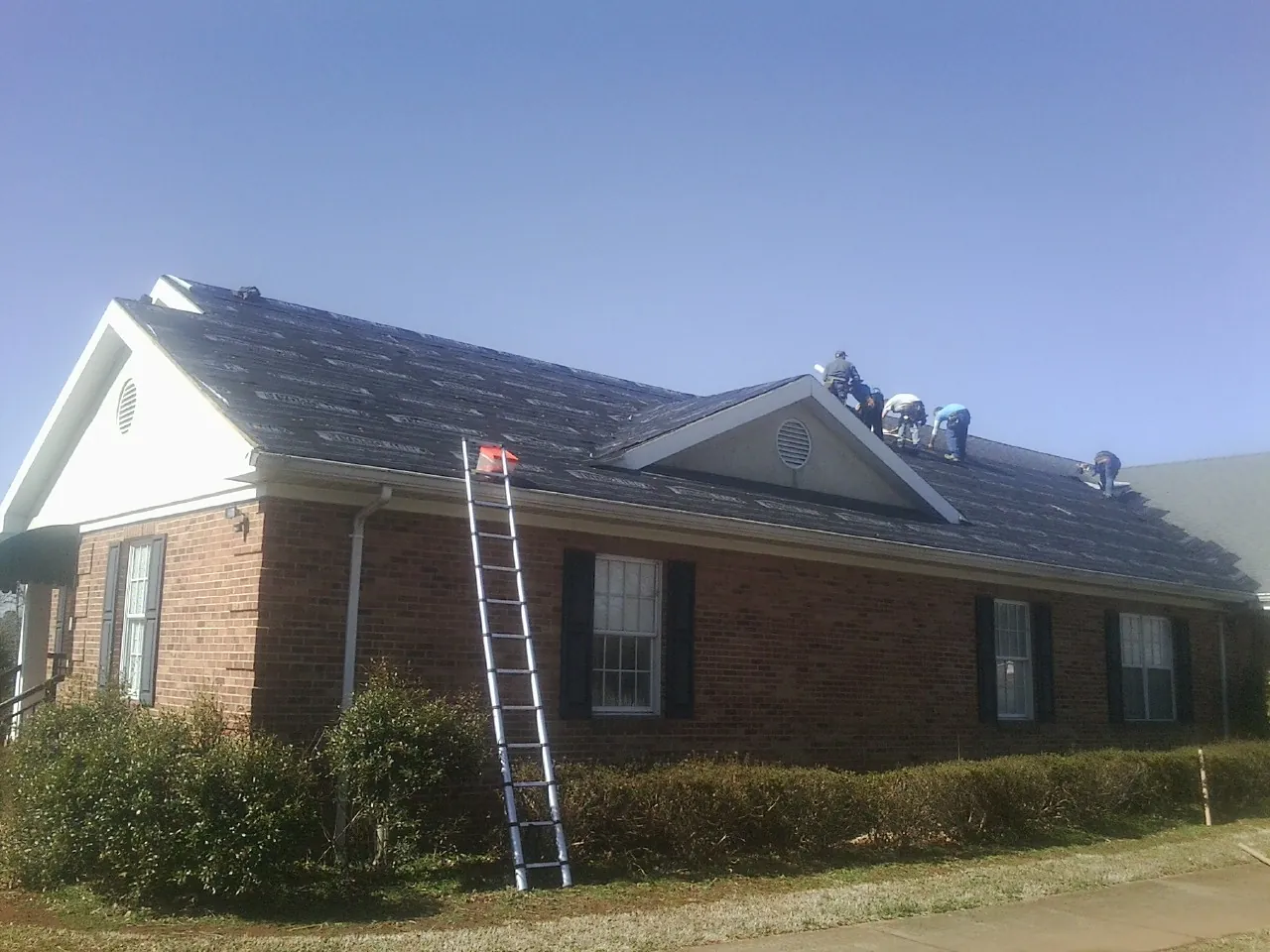 Crew tearing shingles off a brick ranch roof with a ladder set — Metal Roof Repair work by our crew in Madison