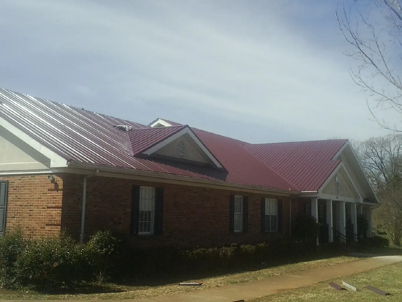 Red metal roof with gabled entries on a long brick building, from a Hail Damage Roof Repair job in Madison